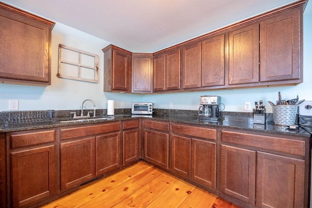 kitchen featuring dark stone countertops, sink, and light hardwood / wood-style flooring