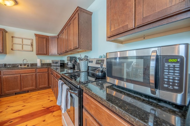 kitchen with stainless steel appliances, sink, light hardwood / wood-style floors, and dark stone counters