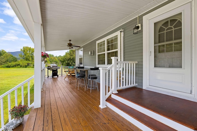 wooden terrace with ceiling fan, area for grilling, and a lawn