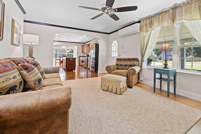 living room with a wall mounted air conditioner, a wealth of natural light, ornamental molding, and light wood-type flooring