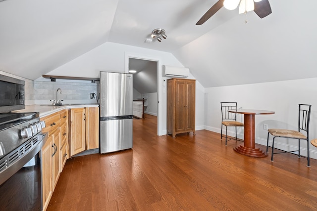 kitchen featuring vaulted ceiling, appliances with stainless steel finishes, a wall mounted air conditioner, wood-type flooring, and sink