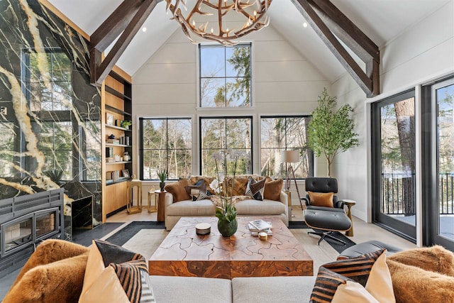 sunroom with a notable chandelier, a wealth of natural light, lofted ceiling with beams, and a premium fireplace