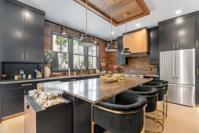 kitchen featuring light stone counters, hanging light fixtures, high end refrigerator, and a kitchen island