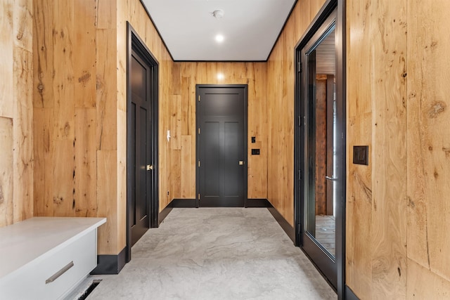 hallway with elevator, wooden walls, and concrete flooring