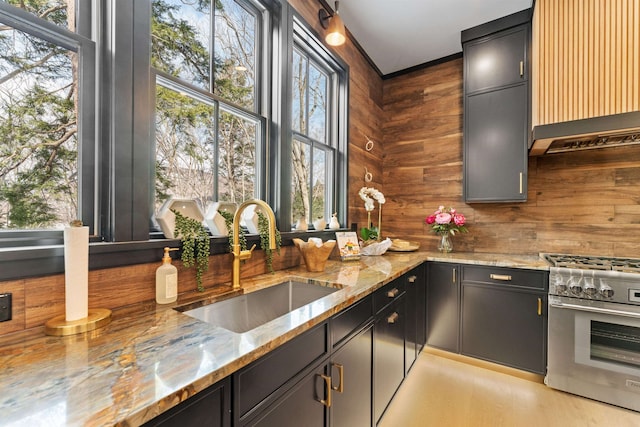 kitchen with high end stainless steel range, sink, custom exhaust hood, wooden walls, and light stone countertops