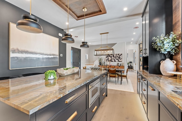 kitchen featuring stainless steel microwave, hanging light fixtures, light stone counters, light hardwood / wood-style floors, and a raised ceiling