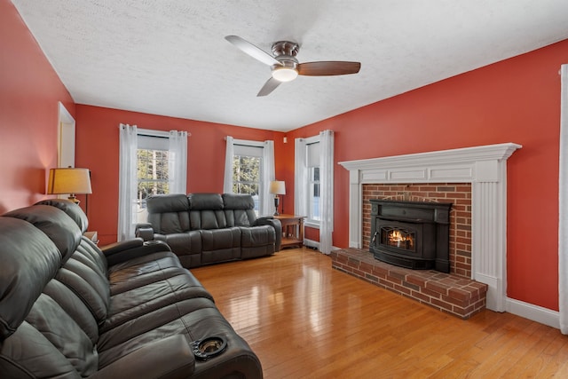 living room featuring a fireplace, light wood-style flooring, ceiling fan, a textured ceiling, and baseboards