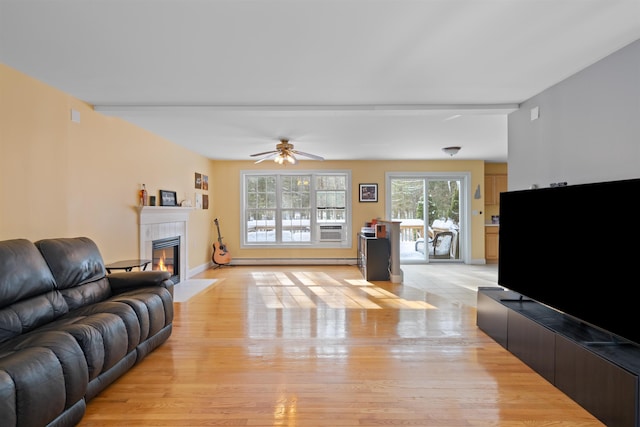 living room with baseboard heating, ceiling fan, light hardwood / wood-style floors, and a tile fireplace