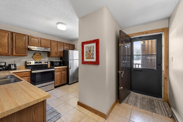 kitchen featuring sink, a textured ceiling, light tile patterned floors, stainless steel appliances, and a baseboard heating unit