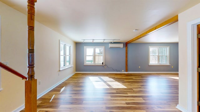 unfurnished room with a wall mounted air conditioner, track lighting, and hardwood / wood-style floors