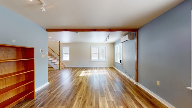 unfurnished living room featuring track lighting, wood-type flooring, and a wall unit AC