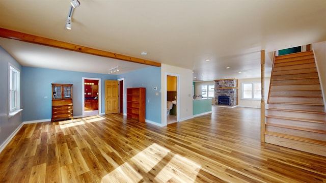 unfurnished living room with beam ceiling, a stone fireplace, track lighting, and light hardwood / wood-style floors