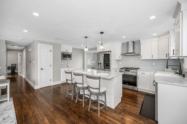 kitchen featuring a kitchen island, appliances with stainless steel finishes, pendant lighting, white cabinets, and wall chimney exhaust hood