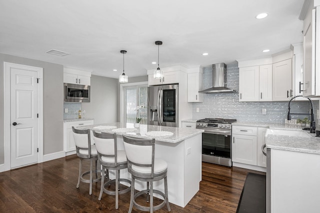 kitchen with wall chimney range hood, sink, appliances with stainless steel finishes, white cabinetry, and a kitchen island