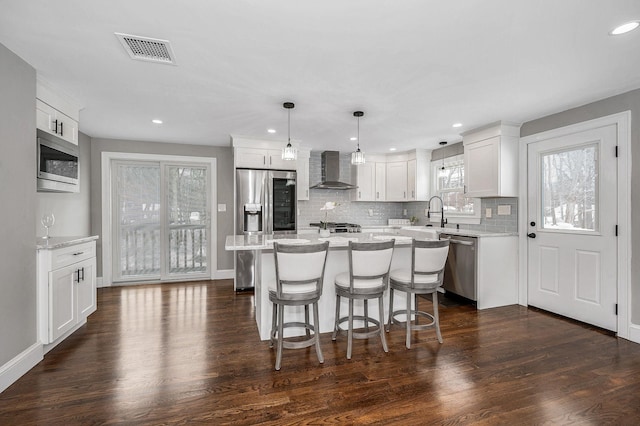 kitchen with pendant lighting, wall chimney range hood, stainless steel appliances, and white cabinets