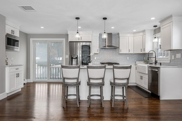 kitchen featuring appliances with stainless steel finishes, white cabinetry, sink, a center island, and wall chimney range hood