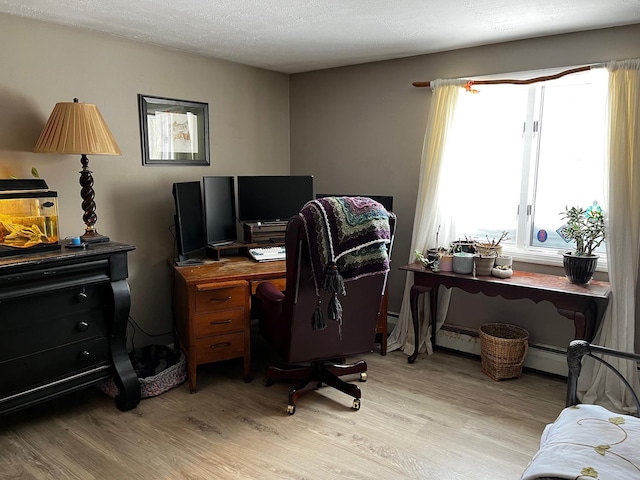 office space featuring light wood-style flooring, a baseboard heating unit, and a textured ceiling