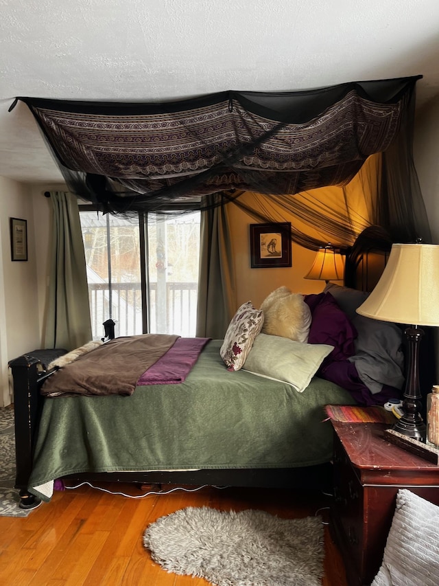 bedroom with access to exterior, a textured ceiling, and wood finished floors