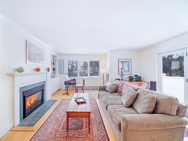 living room with built in shelves, crown molding, light hardwood / wood-style flooring, a tile fireplace, and a baseboard heating unit