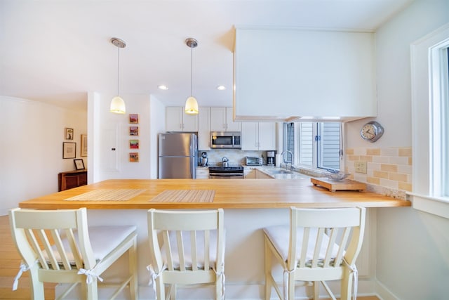 kitchen featuring a breakfast bar, pendant lighting, white cabinetry, kitchen peninsula, and stainless steel appliances