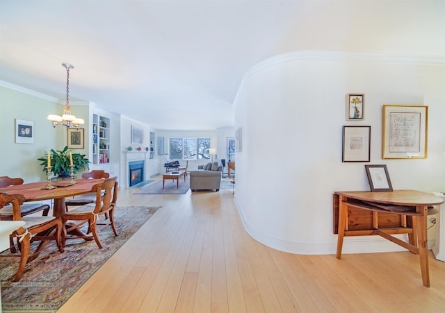 hall featuring built in shelves, a notable chandelier, ornamental molding, and light wood-type flooring