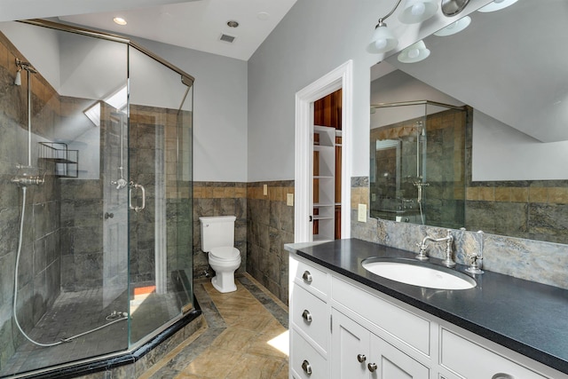 bathroom with toilet, a shower with shower door, vaulted ceiling, tile walls, and vanity