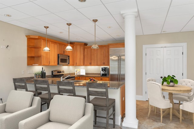 kitchen featuring appliances with stainless steel finishes, hanging light fixtures, decorative columns, a kitchen bar, and kitchen peninsula