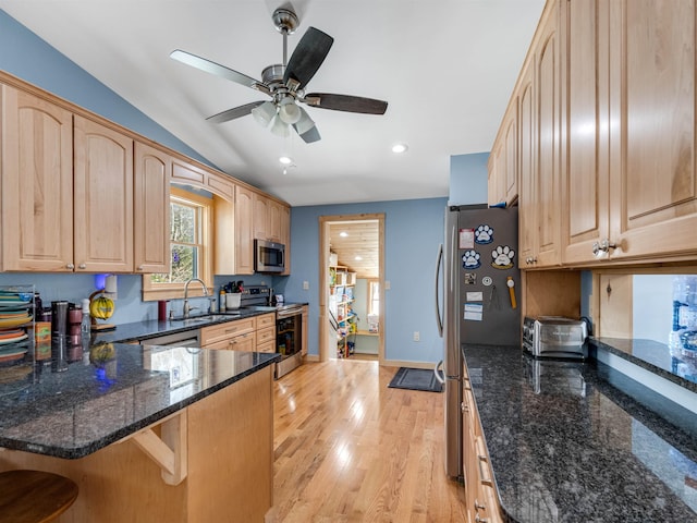 kitchen with appliances with stainless steel finishes, light brown cabinetry, dark stone countertops, sink, and kitchen peninsula