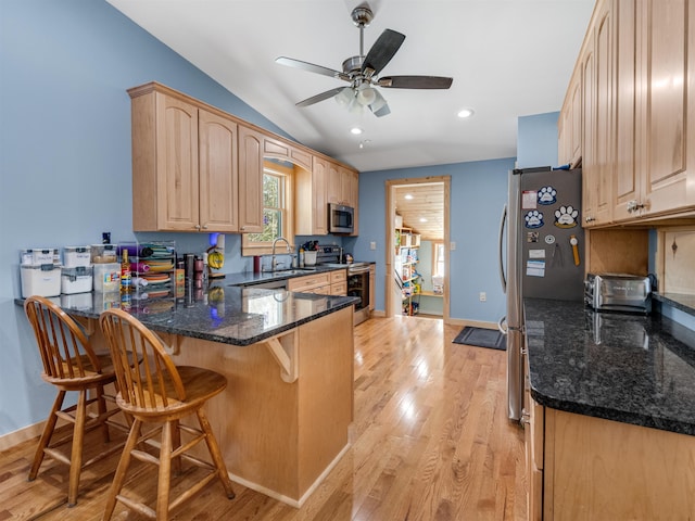 kitchen with kitchen peninsula, appliances with stainless steel finishes, dark stone countertops, and light brown cabinetry