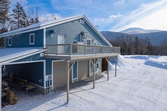 snow covered house with a deck with mountain view and a garage