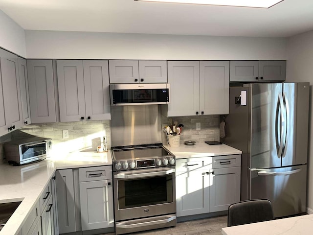 kitchen featuring gray cabinets, light stone countertops, appliances with stainless steel finishes, and decorative backsplash