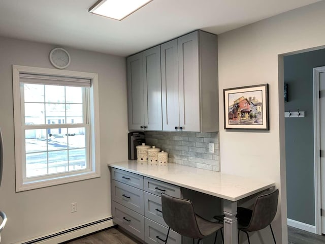 kitchen with a baseboard radiator, gray cabinets, light stone countertops, and backsplash