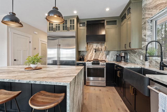 kitchen with premium range hood, appliances with stainless steel finishes, decorative light fixtures, and sink