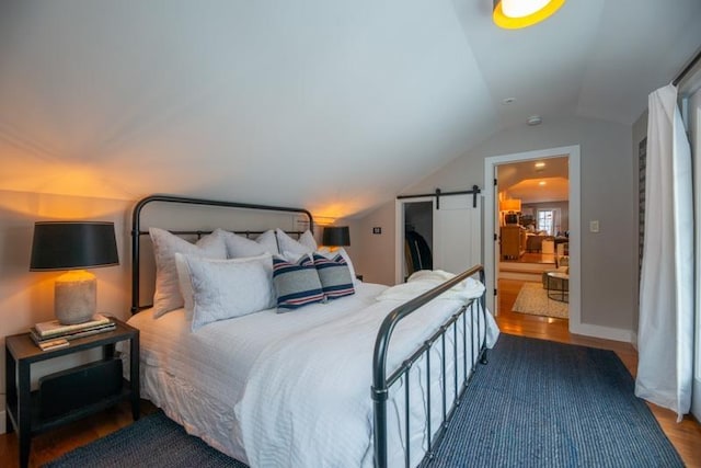 bedroom with vaulted ceiling, connected bathroom, dark hardwood / wood-style flooring, and a barn door