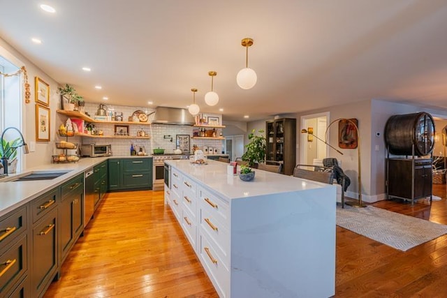 kitchen featuring light wood-type flooring, sink, white cabinets, wall chimney range hood, and pendant lighting