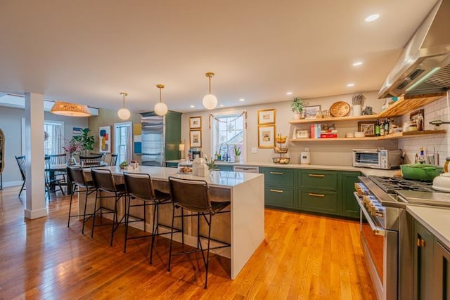 kitchen featuring hanging light fixtures, light hardwood / wood-style floors, extractor fan, high end stove, and a kitchen bar