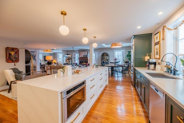 kitchen featuring appliances with stainless steel finishes, sink, light wood-type flooring, white cabinetry, and decorative light fixtures