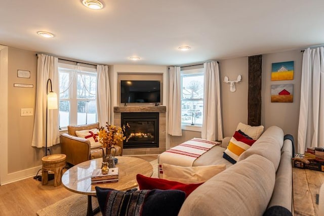 living room with light hardwood / wood-style flooring, a tiled fireplace, and a healthy amount of sunlight