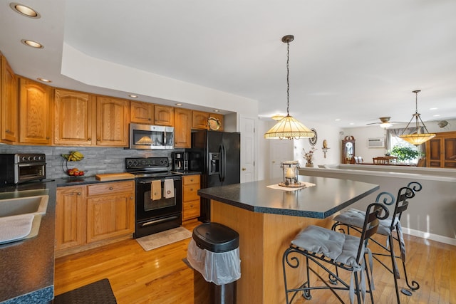 kitchen featuring a kitchen breakfast bar, black appliances, light hardwood / wood-style floors, pendant lighting, and backsplash