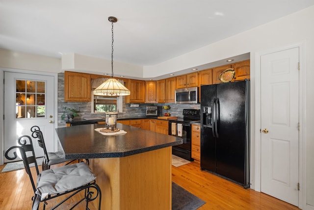 kitchen with light hardwood / wood-style flooring, black appliances, pendant lighting, a breakfast bar, and a center island