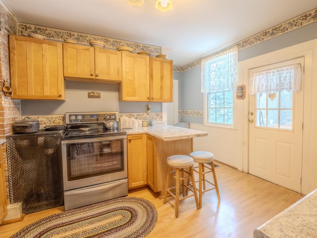 kitchen featuring light brown cabinetry, a breakfast bar area, electric range, light wood-type flooring, and kitchen peninsula