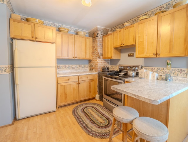 kitchen with light wood-type flooring, kitchen peninsula, white refrigerator, stainless steel range with electric stovetop, and a breakfast bar area