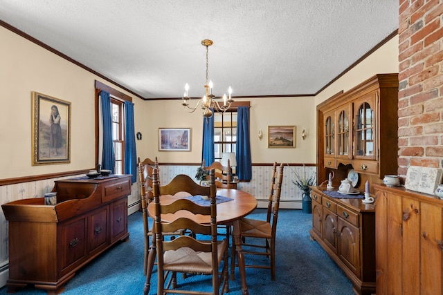 carpeted dining room featuring wooden walls, a textured ceiling, baseboard heating, ornamental molding, and an inviting chandelier