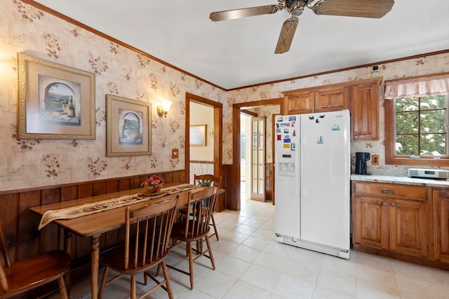 kitchen with ceiling fan, white fridge with ice dispenser, crown molding, and light stone counters