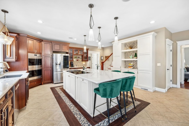 kitchen with appliances with stainless steel finishes, sink, white cabinetry, decorative light fixtures, and a kitchen island with sink