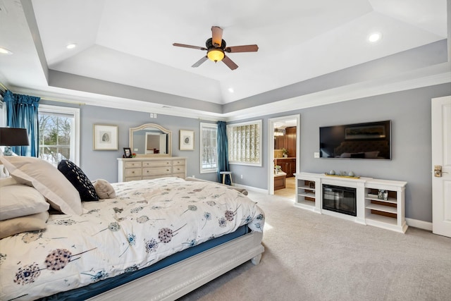 carpeted bedroom featuring a raised ceiling, ensuite bathroom, and ceiling fan