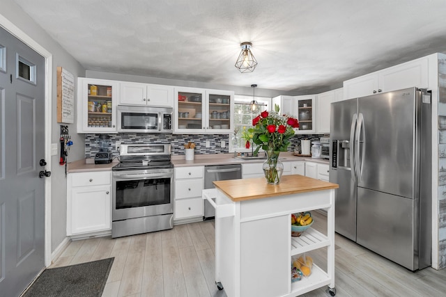 kitchen featuring stainless steel appliances, white cabinets, light hardwood / wood-style floors, pendant lighting, and a center island