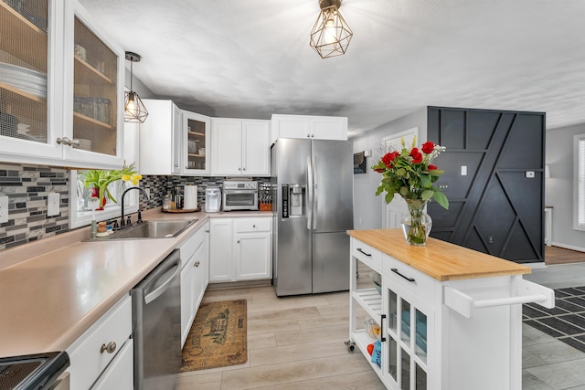 kitchen with hanging light fixtures, sink, backsplash, appliances with stainless steel finishes, and white cabinets