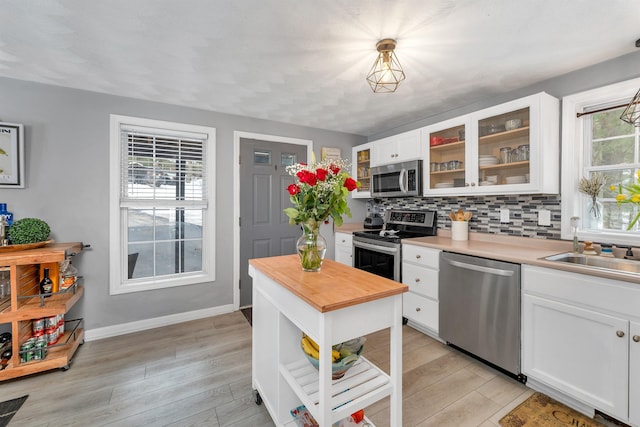 kitchen featuring appliances with stainless steel finishes, light wood-type flooring, white cabinets, and backsplash