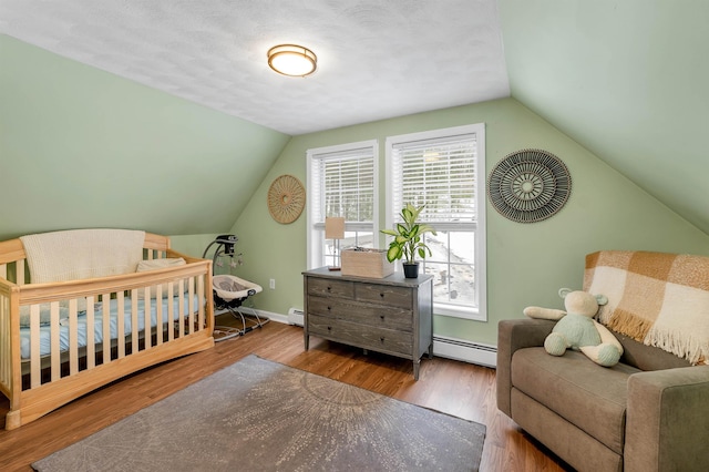 bedroom with a crib, lofted ceiling, hardwood / wood-style floors, and baseboard heating